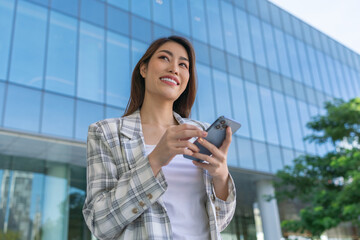 Casual Asian Businesswoman Using Phone In Front A Modern Glass Office Building In The City