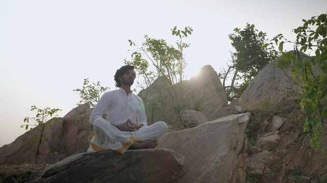 young Indian yogi doing his yoga mediation practices on hills rocks in forest