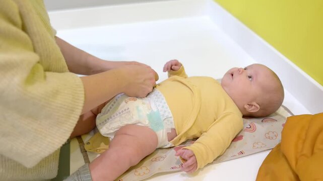 Mom changes the diaper for her newborn baby. Cute two-month-old boy or girl. The infant child looks at her mother attentively during mom to change her baby's nappy