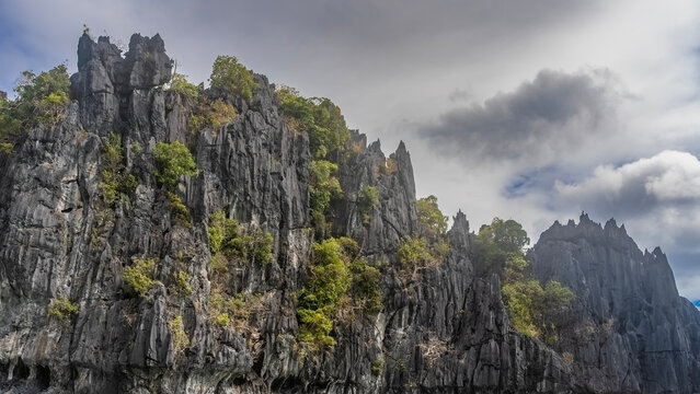 Sheer, inaccessible cliffs against the sky and clouds. There is green tropical vegetation on the steep furrowed slopes. Philippines. Palawan.