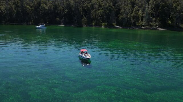 boat with a red canopy floating on the pristine, emerald-green waters of Bah&iacute;a Lynch, located in the Arrayanes Forest, within Nahuel Huapi Lake. Surrounded by lush vegetation and calm waters
