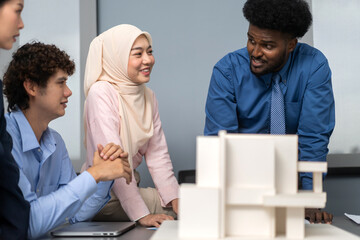 Architects engineers collaborating on building design project in modern office, diverse team of professionals female muslim architect and male engineers discussing architectural model of structure