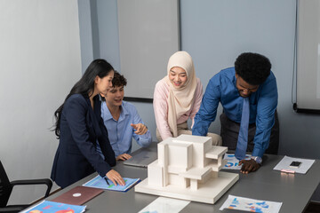 Architects engineers collaborating on building design project in modern office, diverse team of professionals female muslim architect and male engineers discussing architectural model of structure