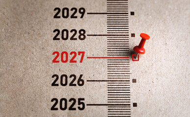 Red pin marks year 2027 on brown paper. Start the new year concept, transition from 2026 to 2027...