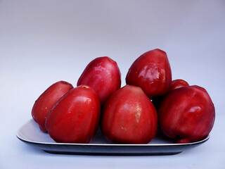 Red rose apple on a plate on a white background; fresh organic red rose apple as a thirst quencher