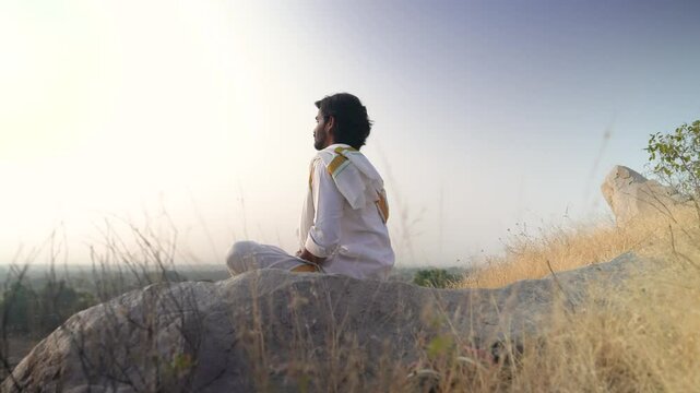 young Indian yogi doing his yoga mediation practices on hills rocks in forest