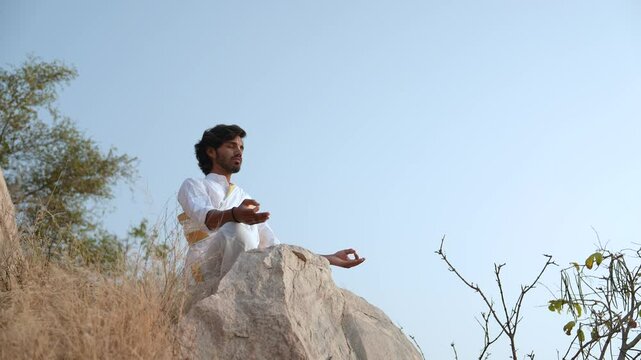 young Indian yogi doing his yoga mediation practices on hills rocks in forest