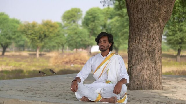 young Indian yogi doing his yoga mediation practices on hills rocks in forest