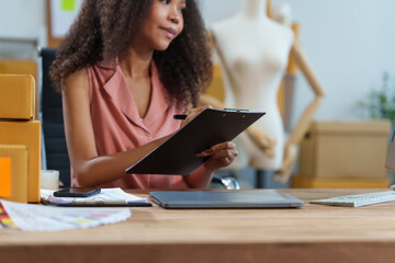 A beautiful African American woman sits at a desk, checking items, packing products, taking orders,...