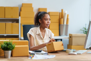 A beautiful African American woman sits at a desk, checking items, packing products, taking orders,...