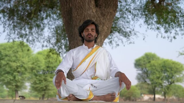 young Indian yogi doing his yoga mediation practices on hills rocks in forest