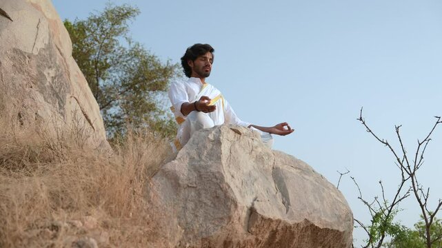 young Indian yogi doing his yoga mediation practices on hills rocks in forest