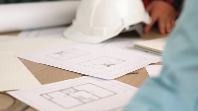 Architect and safety engineer discussion about building blueprint displaying on laptop on table with architectural document and wooden block scatter around at modern office. Closeup. Delineation.