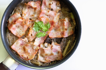 Deliciously cooked bacon on a bed of noodles, garnished with fresh herbs, perfect for food lovers and cooking enthusiasts.