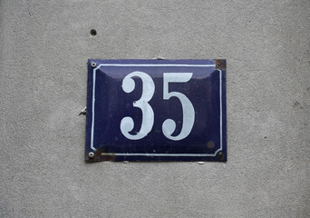 Number 35: White on Blue Metal Plate Against Gray Wall