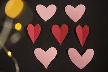corazones de papel acomodados sobre cartulina negra con luz borrosa al frente