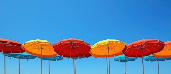 Obraz premium Colorful beach umbrellas against a clear blue sky, creating a vibrant summer atmosphere.
