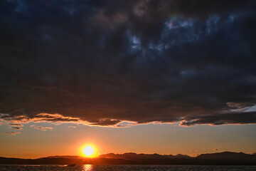 Obraz premium Sunrise over the sea and mountains. Beautiful colorful sunrise at the sea with dramatic clouds and sun shining.