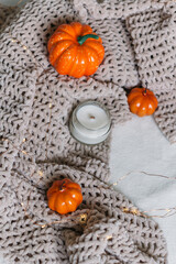 A candle in a glass jar lies on a knitted blanket among orange pumpkins. Autumn decor. Top view