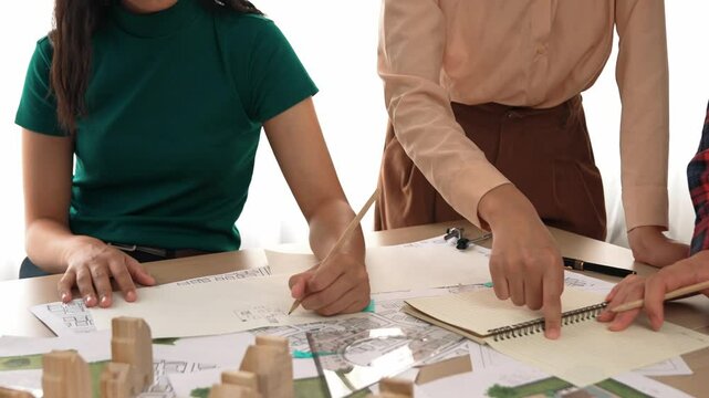 Smart architect and safety engineer discussion about building blueprint on table with architectural document, measurement tools and wooden block scatter around at modern office. Closeup. Delineation.