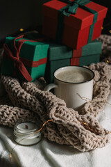 A cup of coffee in a white mug next to a pile of gifts in a plaid. Preparing for Christmas