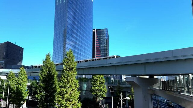 Modern monorail passing tall skyscrapers on a clear sunny day in Tokyo with trees in the foreground