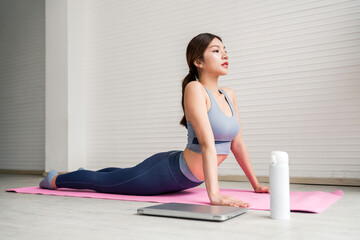 A woman practices yoga on a pink mat, performing the cobra pose in a serene indoor setting, promoting relaxation and wellness.