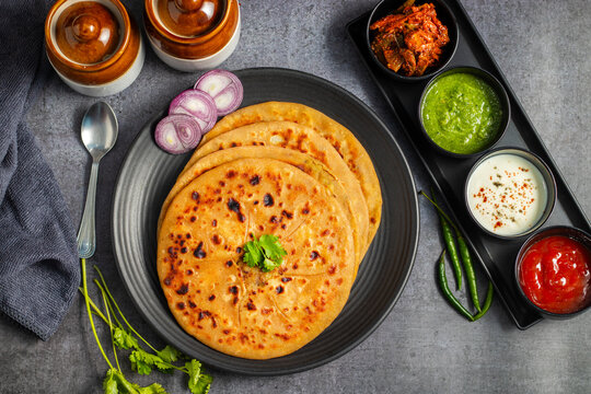 Aloo paratha, a popular North Indian dish, especially in Punjab, is a stuffed flatbread filled with spiced mashed potatoes. It's traditionally served hot with tangy achar (pickle), refreshing chutney,