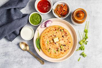 Aloo paratha, a golden-brown Indian flatbread stuffed with spiced mashed potatoes, is served with tangy achar (pickle) and refreshing chutney, creating a perfect blend of flavors for a comforting, sav
