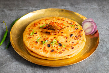 Aloo paratha, a golden-brown Indian flatbread stuffed with spiced mashed potatoes, is served with tangy achar (pickle) and refreshing chutney, creating a perfect blend of flavors for a comforting, sav