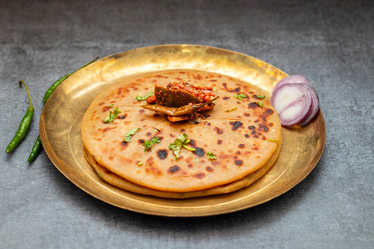 Aloo paratha, a flavorful Indian flatbread stuffed with spiced mashed potatoes, served hot with tangy pickle (achar) and refreshing chutney, creating a perfect balance of zest and warmth.