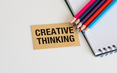 Creative Thinking Text on a card with colored pencils and an open notebook on a white table