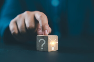Hand touching Glowing light bulb on bright side and question mark on dark side of wooden block cube...