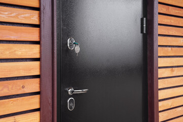 A black door with multiple locks and keyholes is slightly ajar. revealing a sleek wooden wall in...