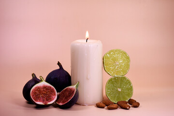 still life with a white candle, ripe figs, lime and almonds against a soft pastel background. The...