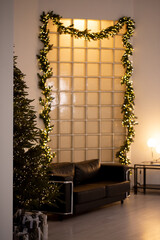 A black couch is in front of a Christmas tree and a partition made of glass blocks. The room is...
