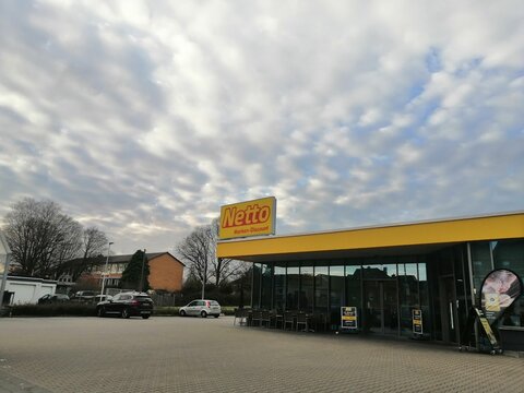 Facade of the Netto Marken Discount supermarket and parking lot under cloudy sky