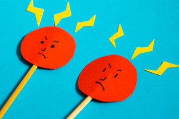 Close up of round angry faces on red colored paper with yellow rays coming out of them on blue background, concept of fury and anger