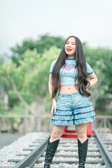 Obraz premium Stylish Young Woman Posing on Railway Tracks in Trendy Outfit, Featuring Denim Shorts and Knee-High Boots, Surrounded by Lush Greenery