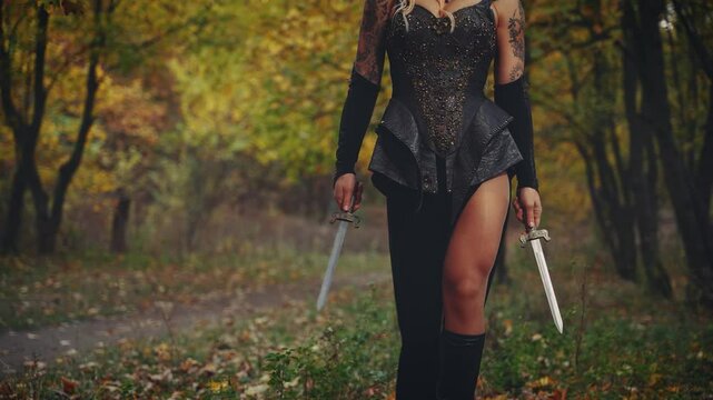 fantasy woman warrior queen holding two sharp knife blade dagger. Fairy girl elf walking in dark night forest autumn nature tree. Black leather creative design dress, lady sexy body part art video 4k