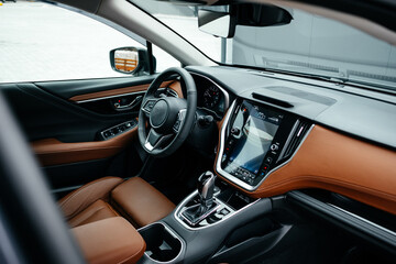 Modern brown car interior, leather steering wheel, climate control, large navigation screen, air ducts, deflectors on the car panel. Interior details.