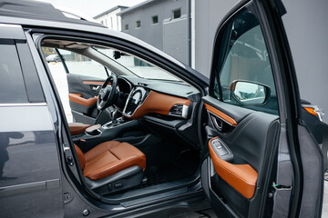 Modern brown car interior, leather steering wheel, climate control, large navigation screen, air ducts, deflectors on the car panel. Interior details.