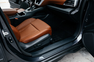 Modern brown car interior, leather steering wheel, climate control, large navigation screen, air ducts, deflectors on the car panel. Interior details.