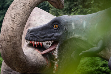 A close up of a dinosaur sculpture in a park, showcasing its detailed design, vibrant colors, and...