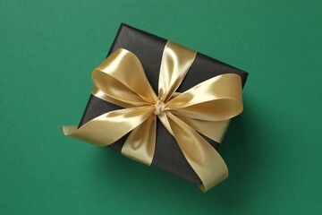 Beautiful gift box tied with golden bow on color background 