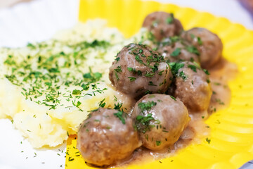 A yellow plate with meatballs and mashed potatoes