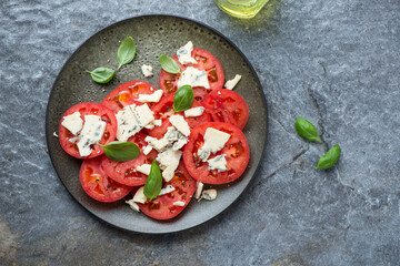 Plate with tomato and blue cheese salad on a dark-grey granite background, horizontal shot, flat lay