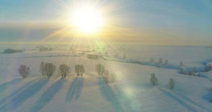 Drone aerial view of cold winter landscape arctic field, trees covered with frost snow, ice river and sun rays over horizon. Extreme low temperature weather.
