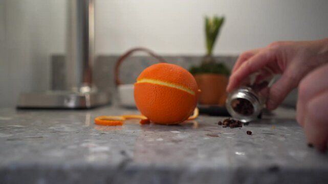 Orange pomander with female hands adding cloves on grey countertop