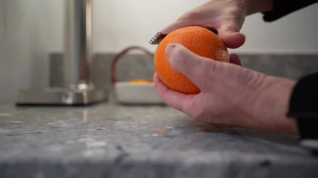 Orange pomander carved with citrus zester by female hands on grey countertop